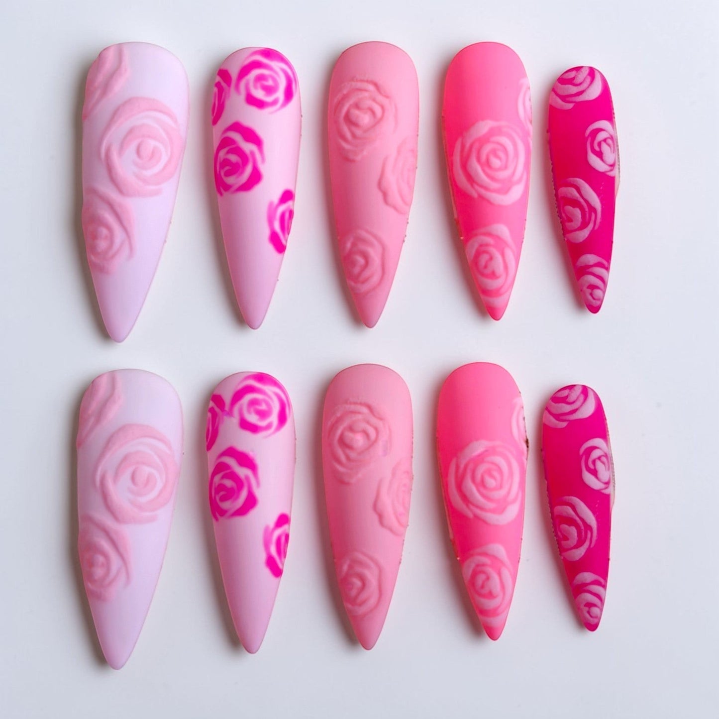 Auntie Cookies Nails almond-shaped press-on nails with a matte pink gradient and 3D embossed rose floral patterns.