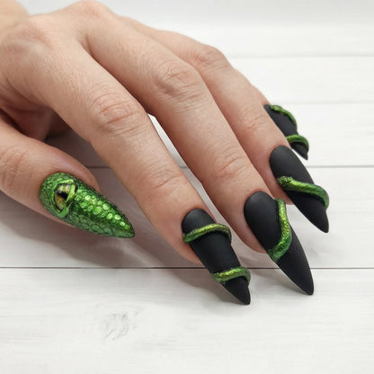Auntie Cookies Nails: Matte black stiletto press-on nails with green chrome snake details and one dragon eye nail.