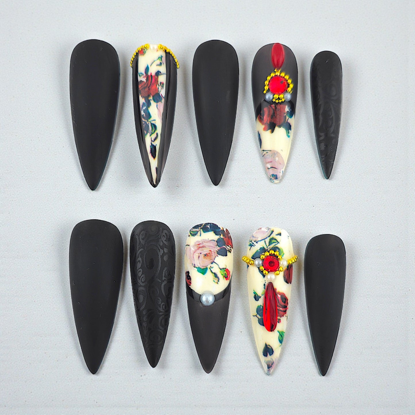 Auntie Cookies Nails: Almond-shaped press-on nails with black matte finish, floral print, red gems, pearls, and gold accents.