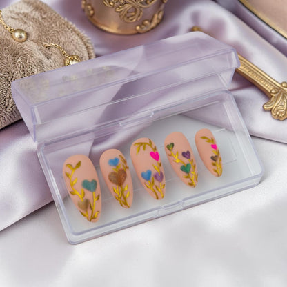 Auntie Cookies Nails: Set of 10 nude press-on nails with gold vine design and heart-shaped tips in pink, blue, purple, and green.