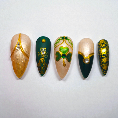 Auntie Cookies Nails: Emerald green, champagne, and gold press-on nails with Celtic knot, clover, and rhinestone details.