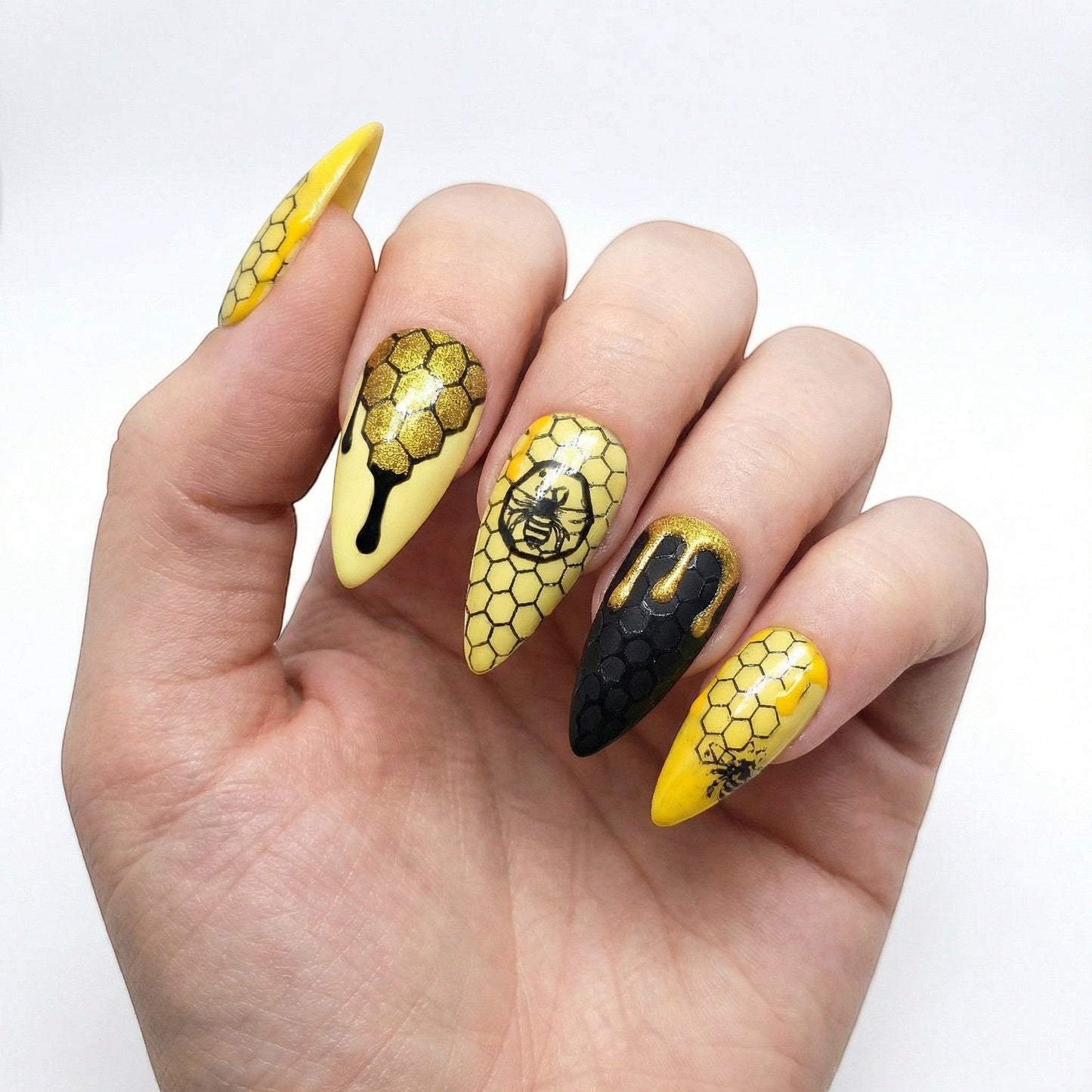 Auntie Cookies Nails: Almond-shaped press-on nails with yellow and black honeycomb pattern, bee designs, and dripping honey accents.