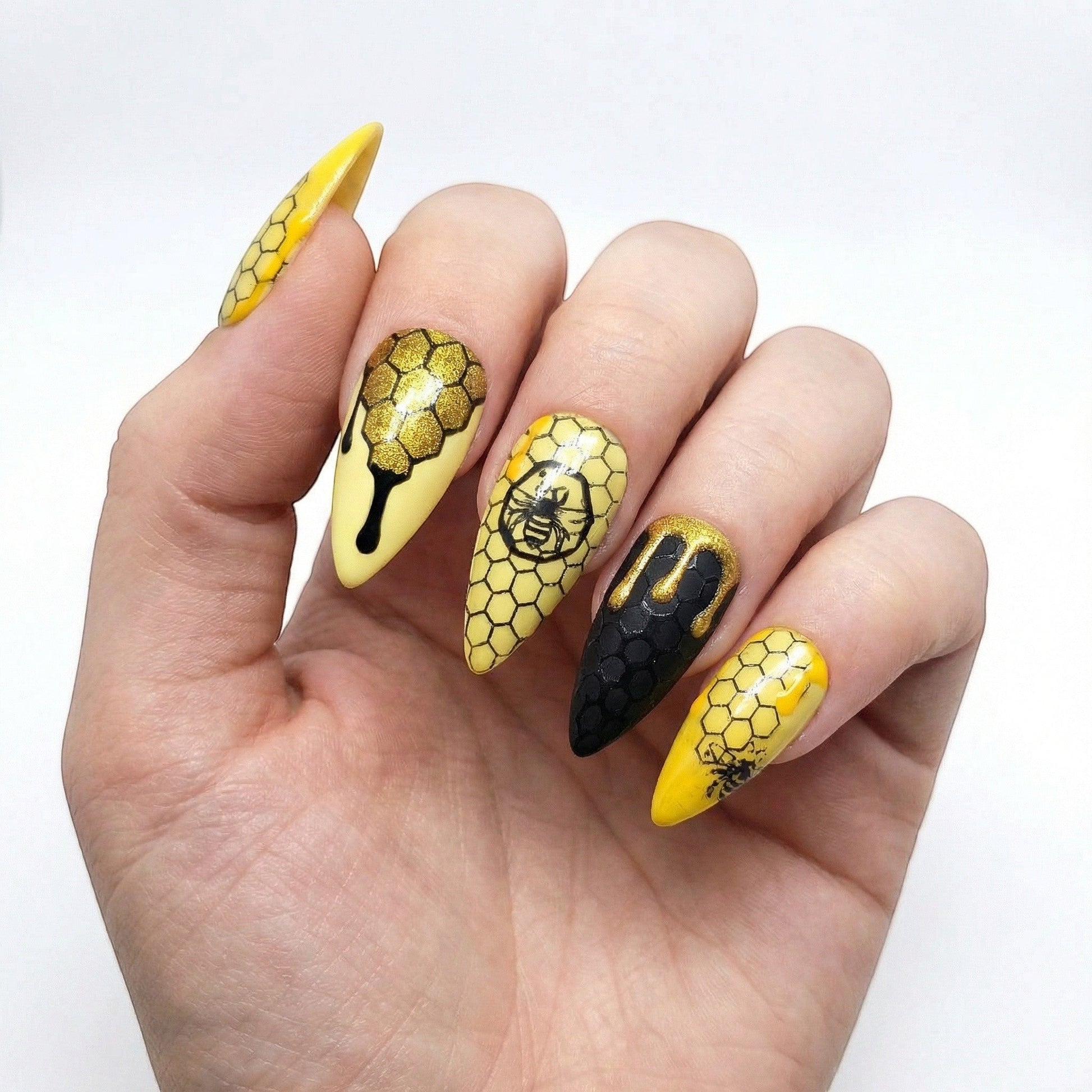 Auntie Cookies Nails: Almond-shaped press-on nails with yellow and black honeycomb pattern, bee designs, and dripping honey accents.