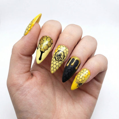Auntie Cookies Nails: Almond-shaped press-on nails with yellow and black honeycomb pattern, bee designs, and dripping honey accents.