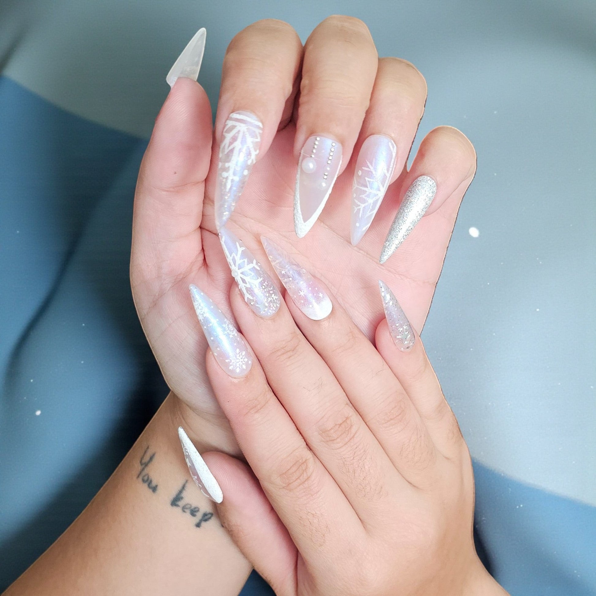 Auntie Cookies Nails Ice Queen stiletto press on nails with snowflake designs, glitter, and pearls in icy blue, silver, and white.