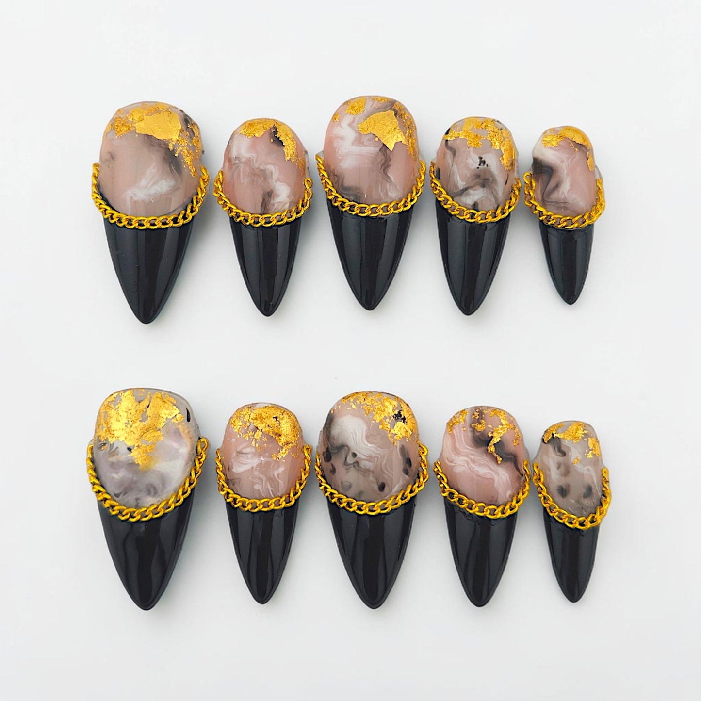 Auntie Cookies Nails almond-stiletto press-on set with marble swirl, black tips, gold leaf, and metallic chain accents.