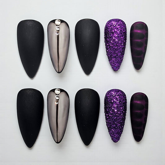 Auntie Cookies Nails: Almond-shaped press-on nails in matte black, chrome with rhinestones, purple glitter, and dark purple stripes.