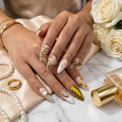 Auntie Cookies Nails Opulent Ivory press on nails with gold heart designs, pearls, and textured accents on stiletto tips.