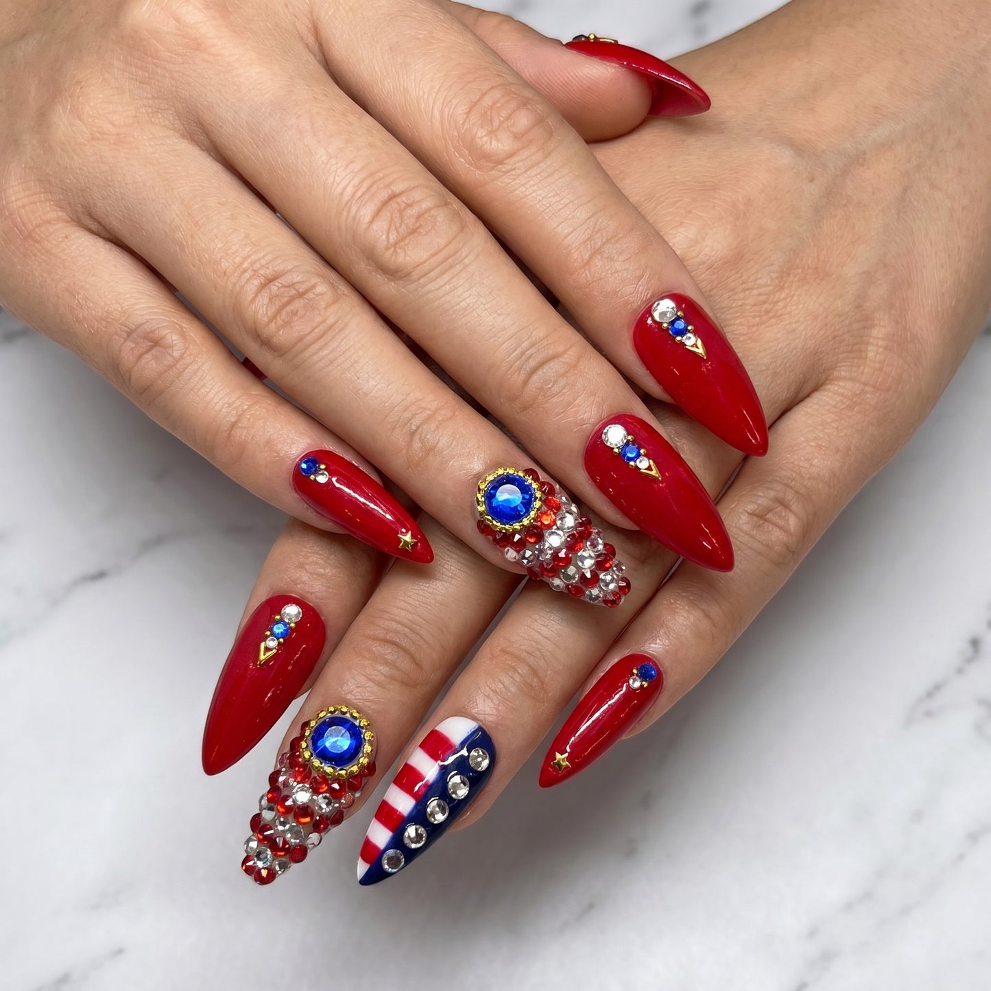 Auntie Cookies Nails stiletto press-on nails in glossy red with American flag accents, rhinestones, and gold star details.
