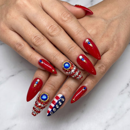 Auntie Cookies Nails stiletto press-on nails in glossy red with American flag accents, rhinestones, and gold star details.