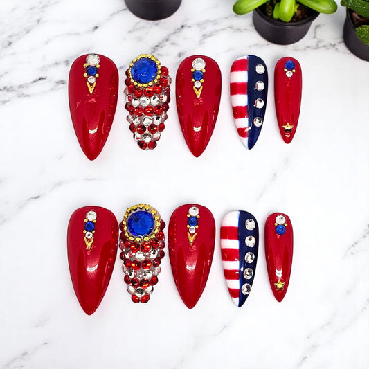 Auntie Cookies Nails stiletto press-on nails in red, white, and blue with rhinestone, crystal, and gold star accents.