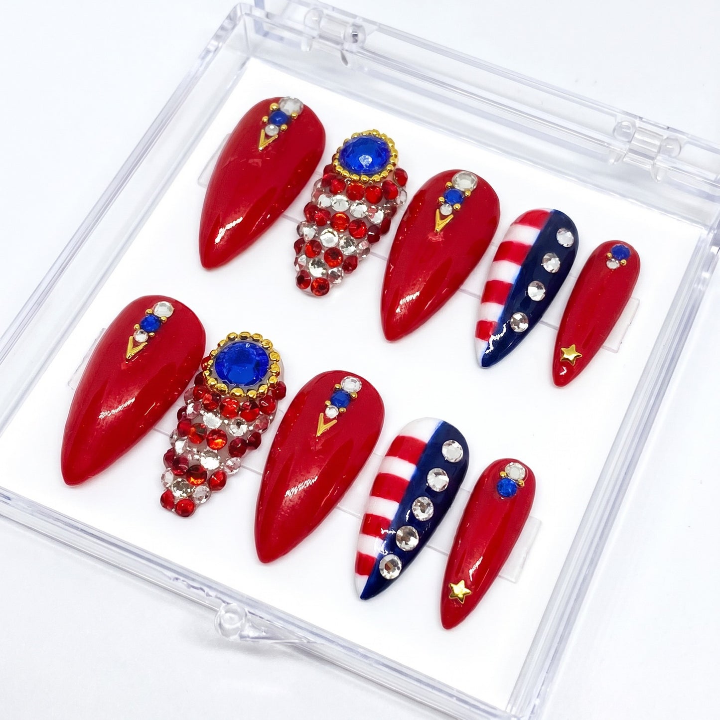Auntie Cookies Nails stiletto press-on nails in red, white, and blue with rhinestones, crystals, and gold star accents.