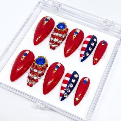 Auntie Cookies Nails stiletto press-on nails in red, white, and blue with rhinestones, crystals, and gold star accents.