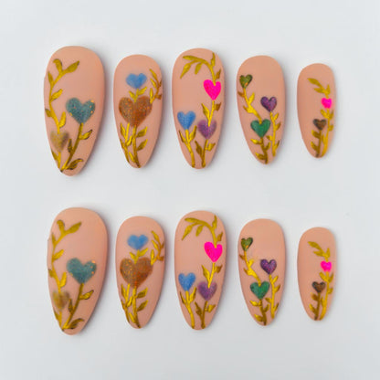 Auntie Cookies Nails: Set of 5 press-on nails in a light peach hue with gold vine accents and colorful heart-shaped flowers.