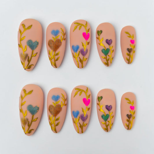 Auntie Cookies Nails: Set of 5 press-on nails in a light peach hue with gold vine accents and colorful heart-shaped flowers.