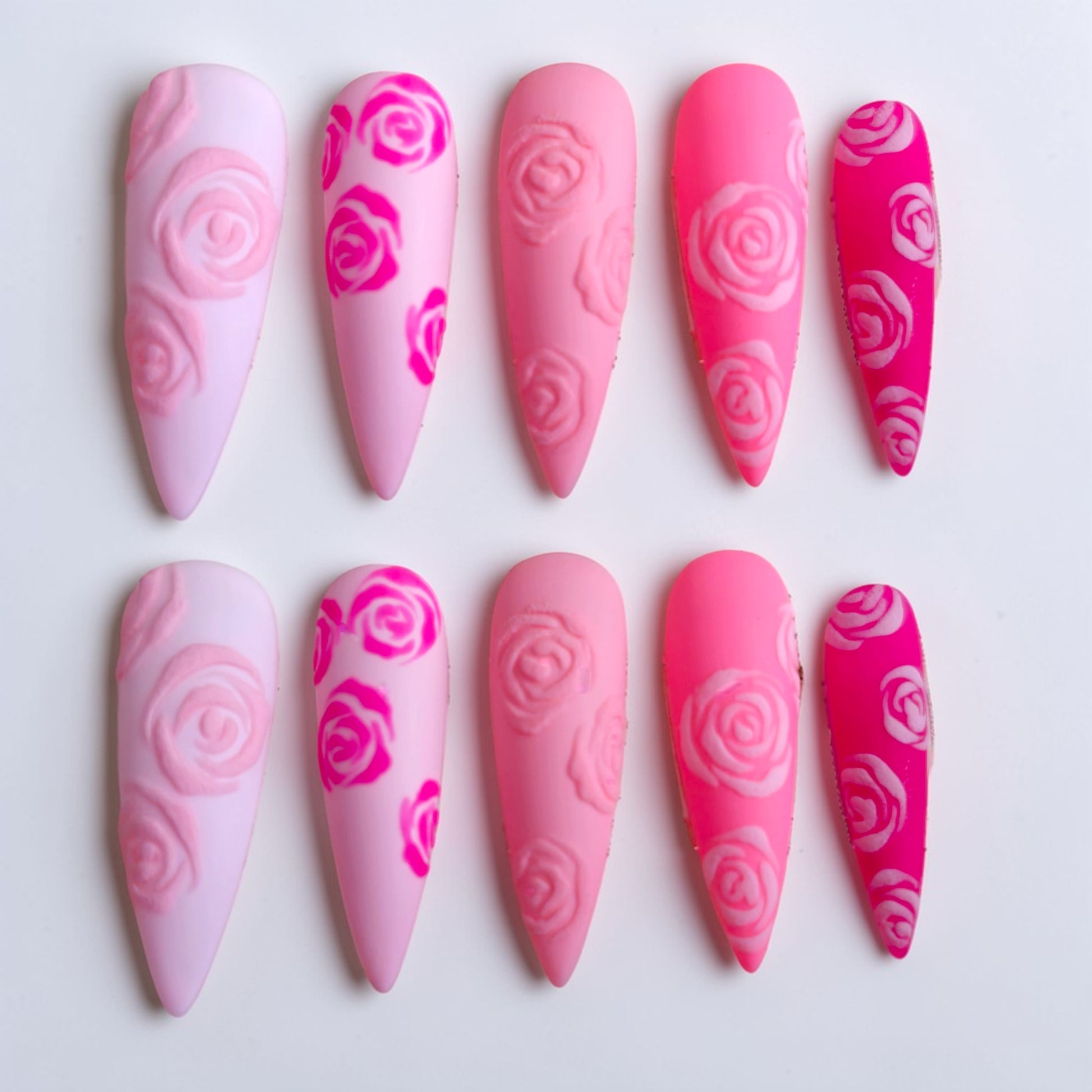 Auntie Cookies Nails: Set of 5 pink press-on nails with rose designs in varying shades of pink and hot pink.