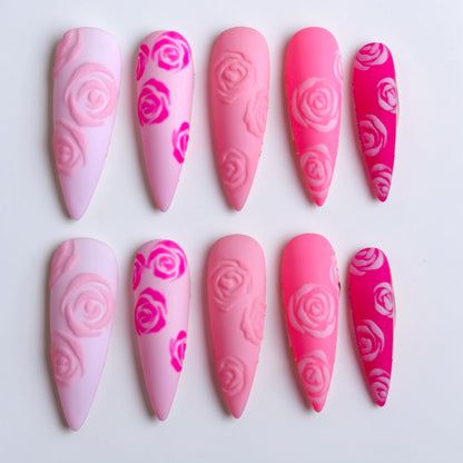 Auntie Cookies Nails: Set of 5 pink press-on nails with rose designs in varying shades of pink and hot pink.