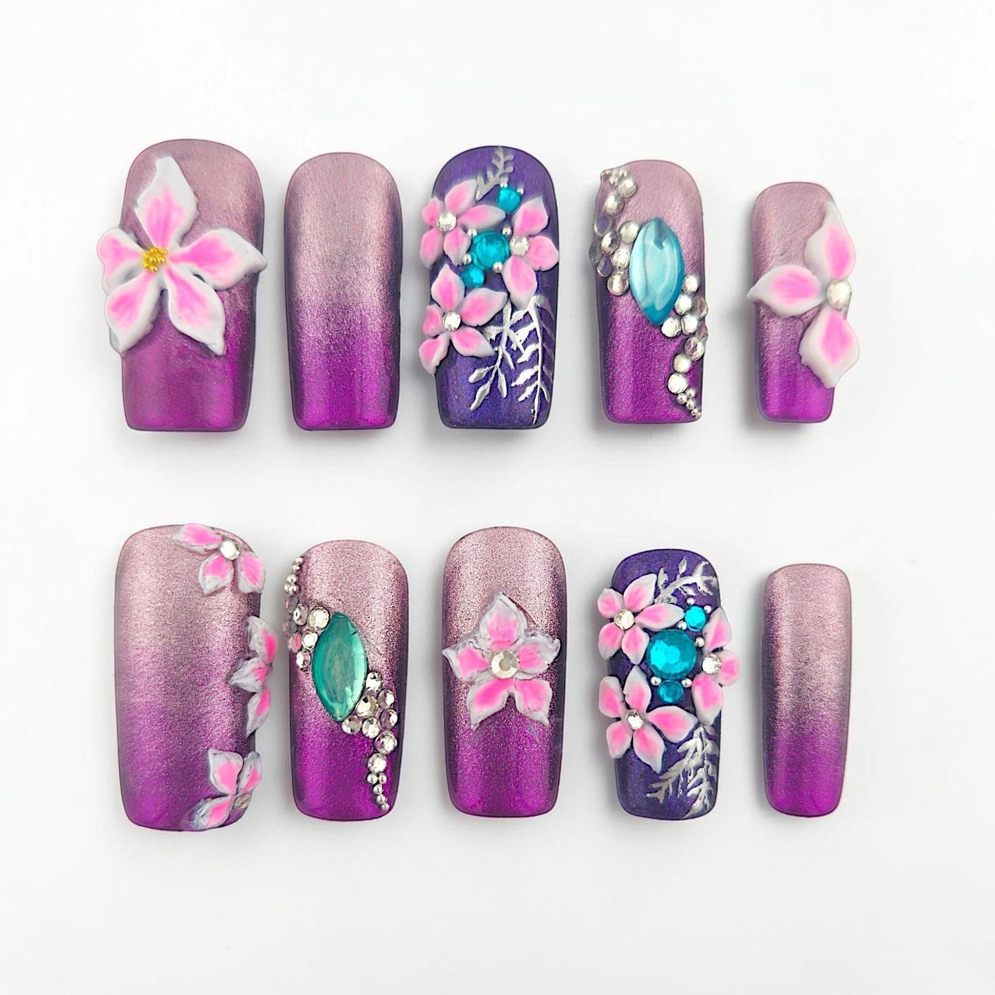 Auntie Cookies Nails: Purple and rose gold gradient press-on nails with 3D pink flowers, turquoise gems, and silver leaf accents.