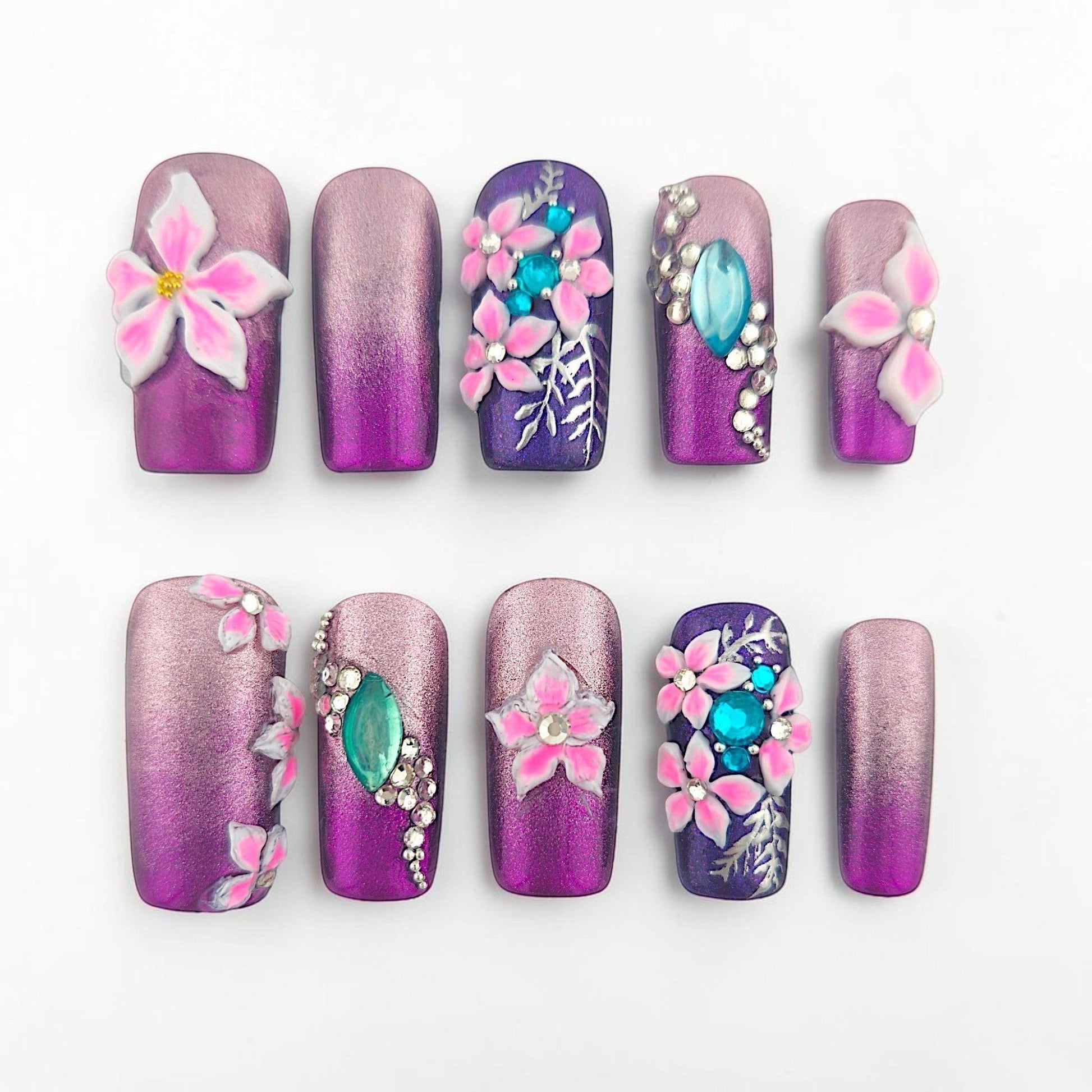 Auntie Cookies Nails: Purple and rose gold gradient press-on nails with 3D pink flowers, turquoise gems, and silver leaf accents.