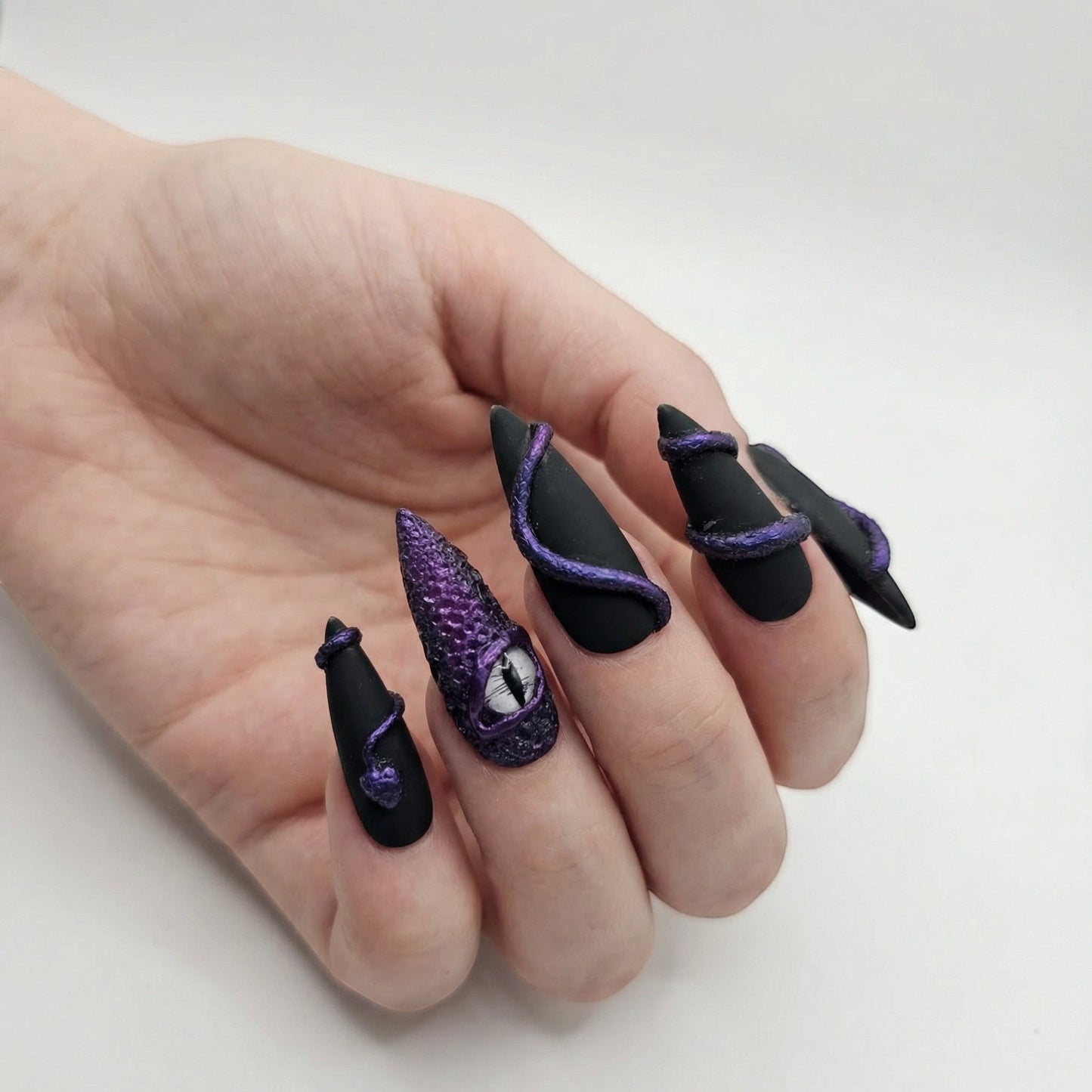 Auntie Cookies Nails matte black stiletto press-on nails with purple serpent details and a dragon eye accent nail.
