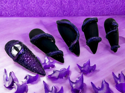 Auntie Cookies Nails: Black coffin press-on nails with purple snake wrap detail and one with a dragon eye.