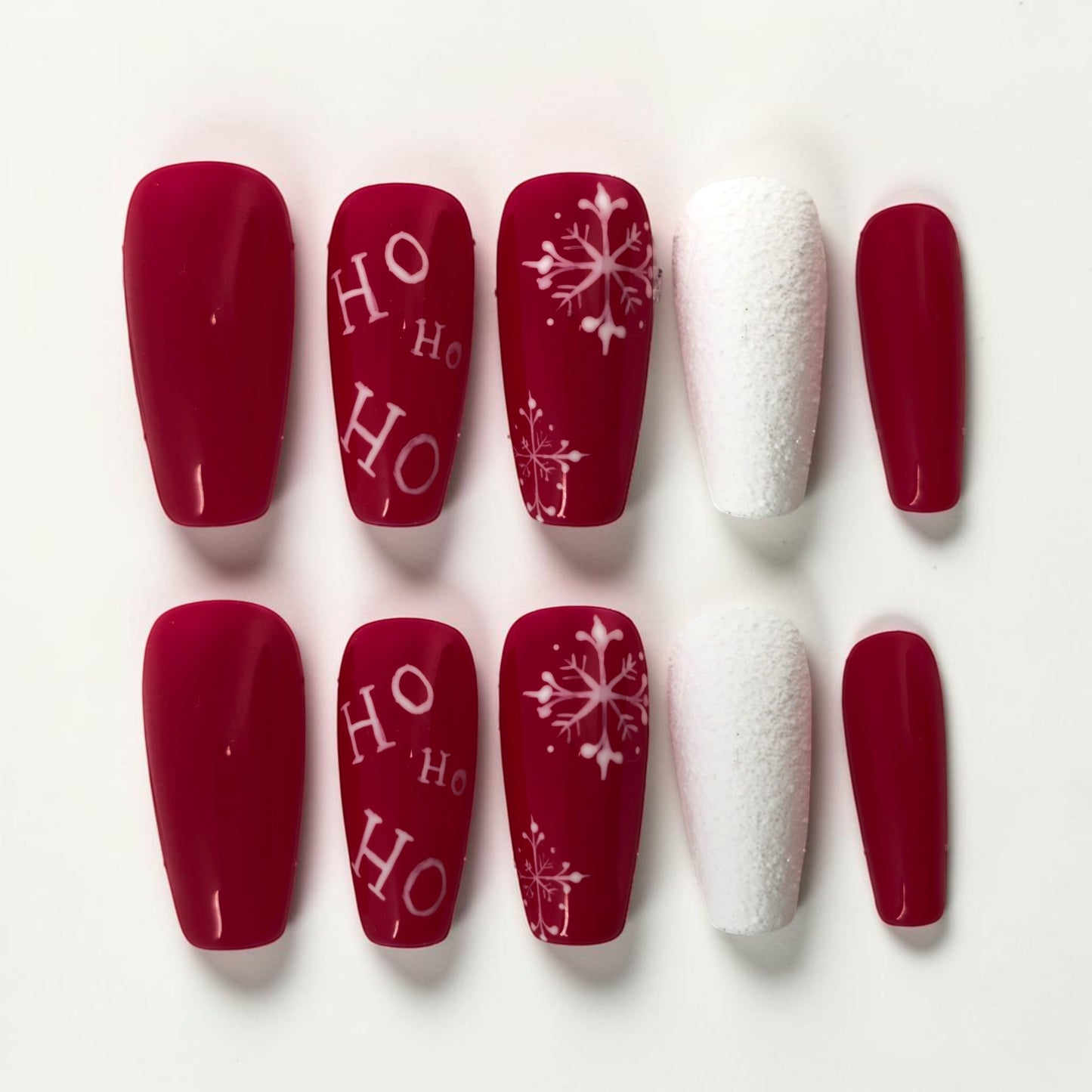 Auntie Cookies Nails festive red press-on nails with white "HO HO HO" text and snowflake designs, plus textured white accent nails.
