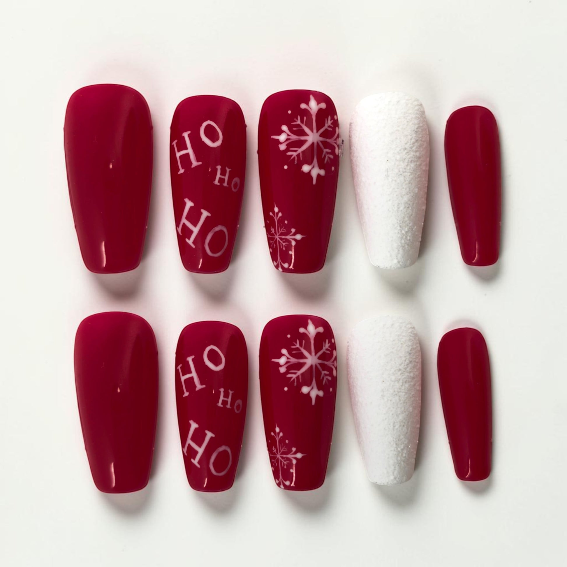 Auntie Cookies Nails festive red press-on nails with white "HO HO HO" text and snowflake designs, plus textured white accent nails.