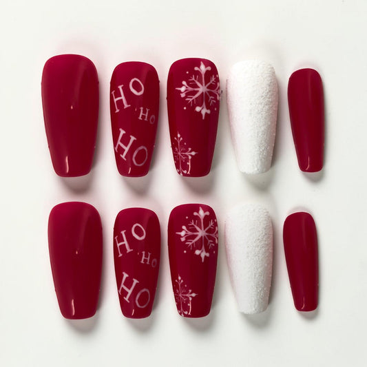 Auntie Cookies Nails festive red press-on nails with white "HO HO HO" text and snowflake designs, plus textured white accent nails.