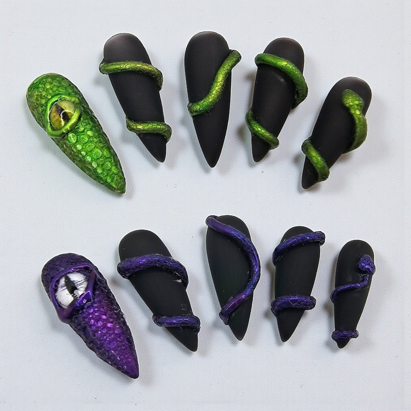 Auntie Cookies Nails: Set of 10 matte black press-on nails with 3D green and purple serpent details and dragon eye accents.