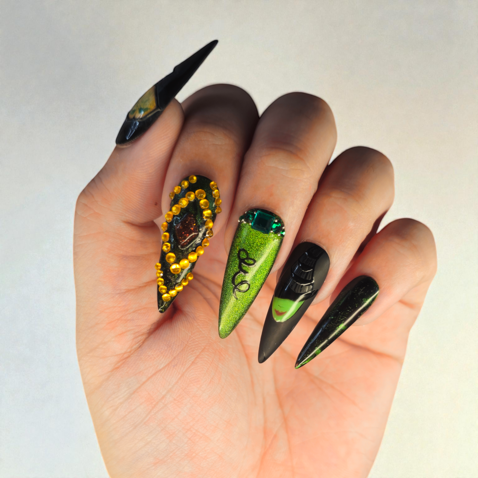 Auntie Cookies Nails: Set of 5 stiletto press-on nails in black and metallic green, adorned with rhinestones and gems.