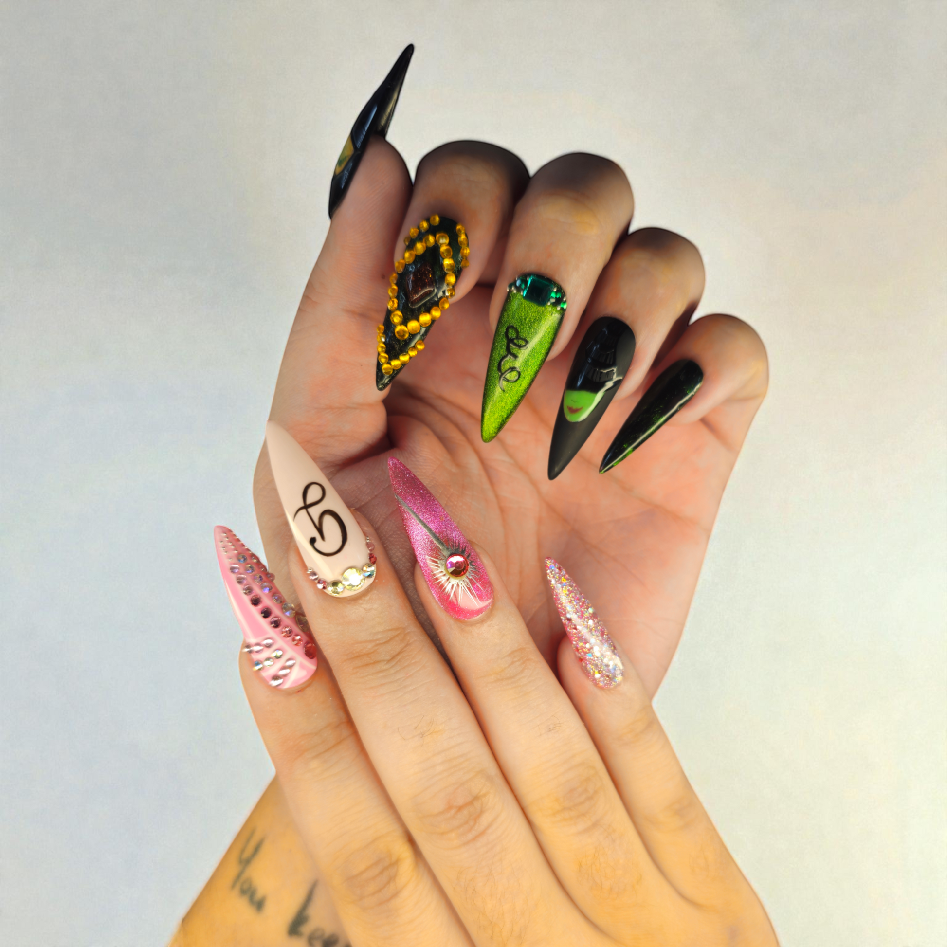 Auntie Cookies Nails: Assortment of long, stiletto-shaped press-on nails in various designs including pink with rhinestones, glitter, green with swirls, and black with accents.