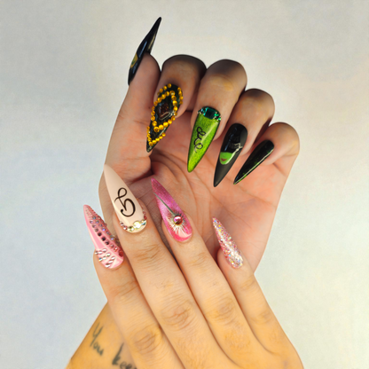 Auntie Cookies Nails: Assortment of long, stiletto-shaped press-on nails in various designs including pink with rhinestones, glitter, green with swirls, and black with accents.