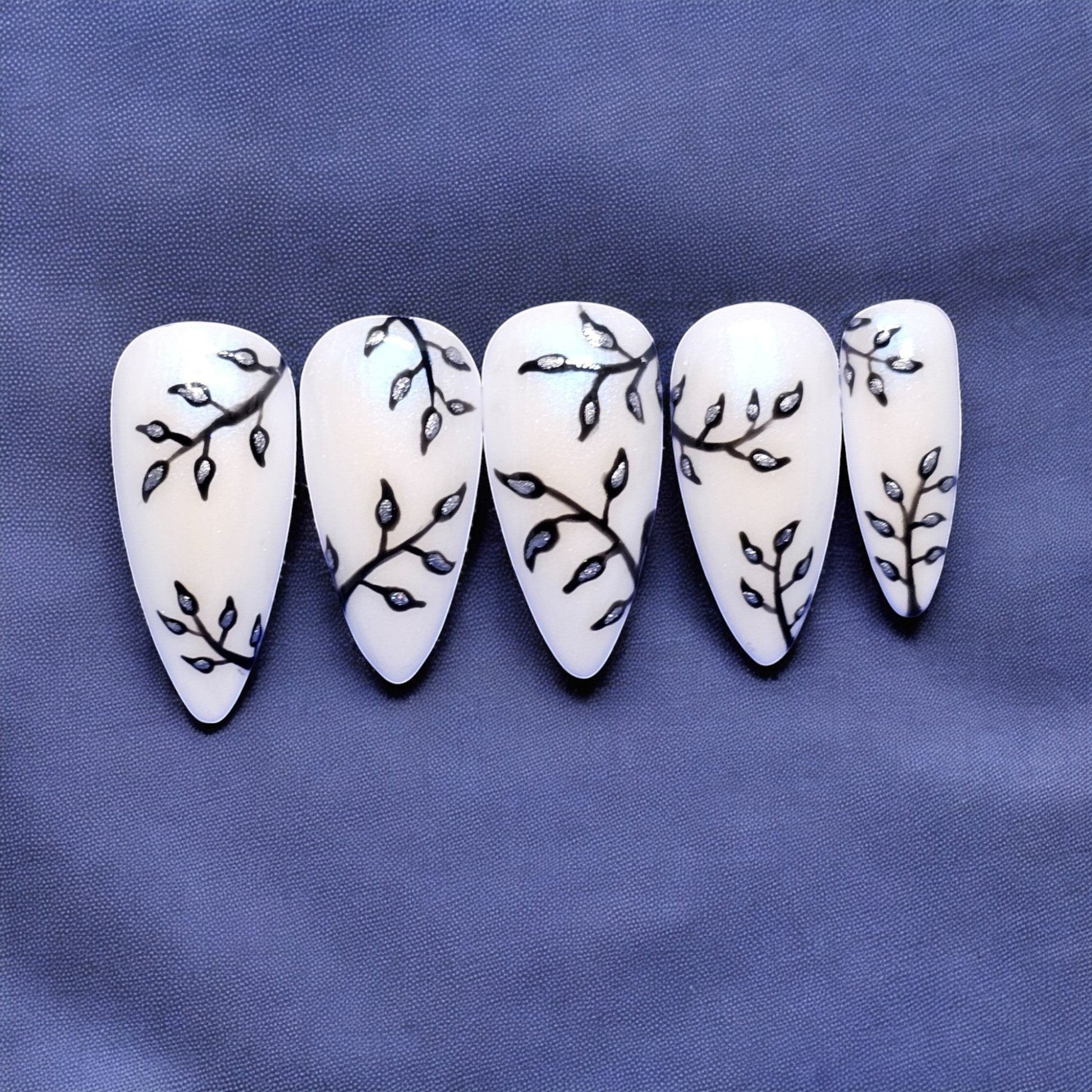 Auntie Cookies Nails shimmery white stiletto press-on nails with black branch and silver leaf design.