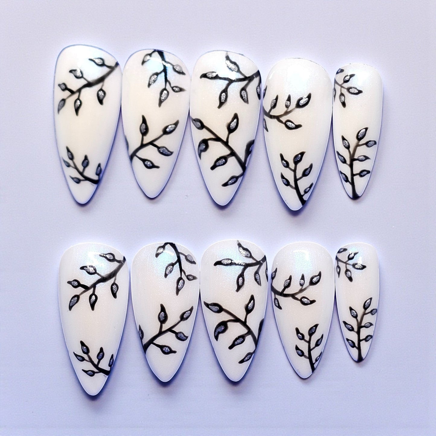 Auntie Cookies Nails: White stiletto press-on nails with black branch and silver leaf design. Medium length.