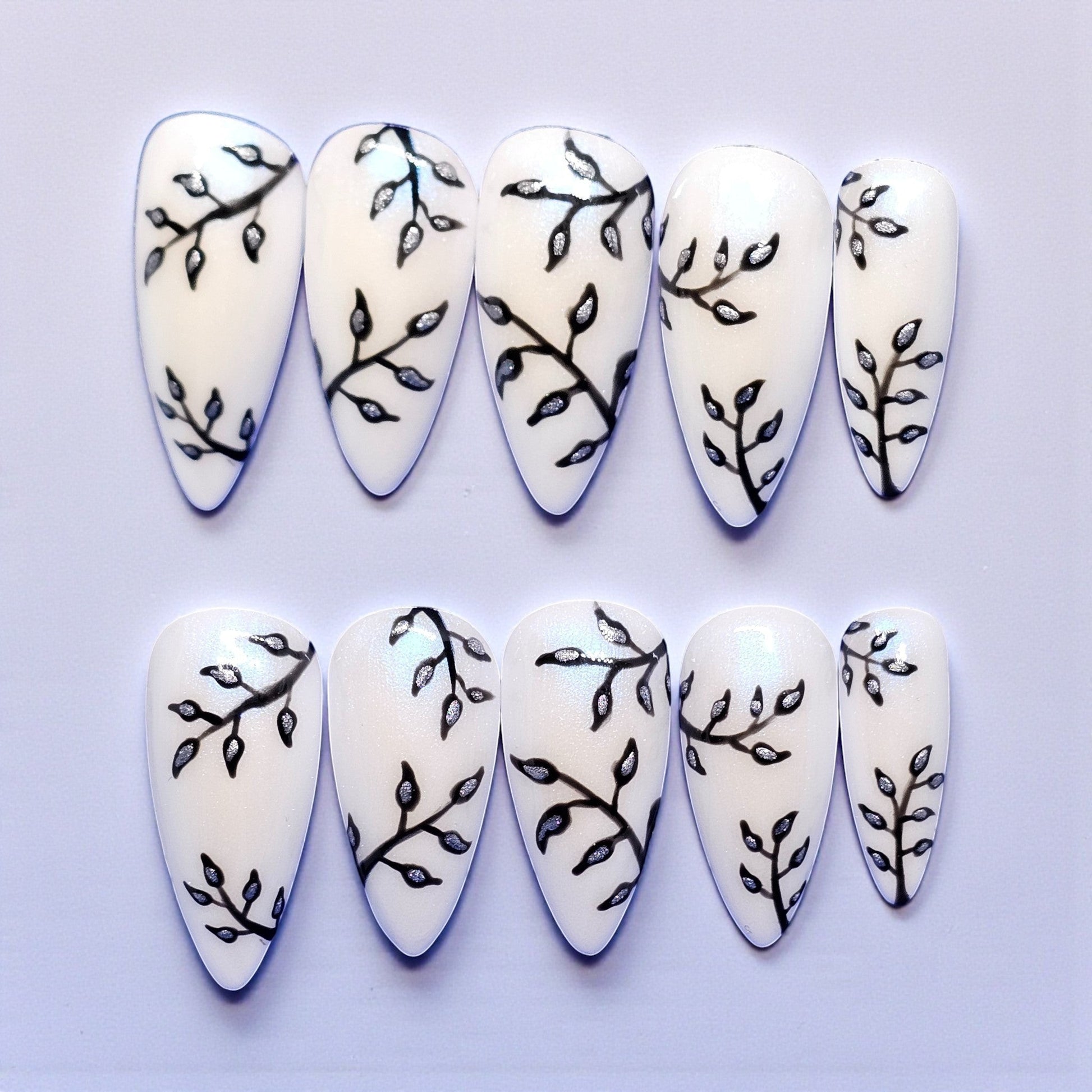 Auntie Cookies Nails: White stiletto press-on nails with black branch and silver leaf design. Medium length.