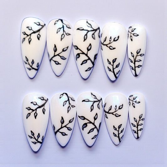 Auntie Cookies Nails: White stiletto press-on nails with black branch and silver leaf design. Medium length.
