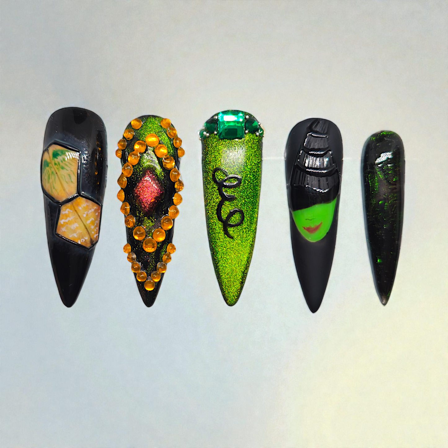 Auntie Cookies Nails: Set of 5 black and green press-on nails with unique designs including gems, glitter, and a witch face.