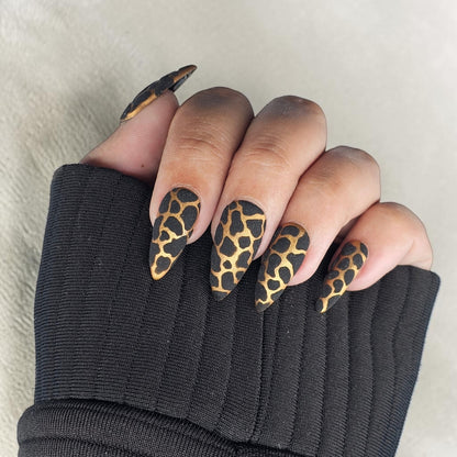 Auntie Cookies Nails: Stiletto press-on nails with black and gold giraffe print and glitter finish.