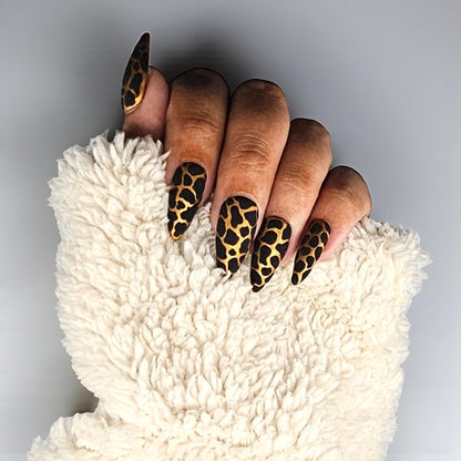 Auntie Cookies Nails stiletto press on nails with black and gold giraffe print and glitter finish.