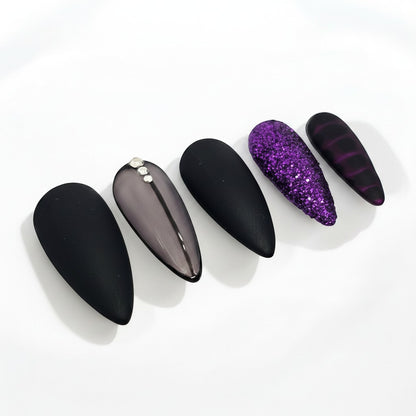 Auntie Cookies Nails: Almond-shaped press-on nails in matte black, sheer grey with rhinestones, purple glitter, and dark purple stripes.