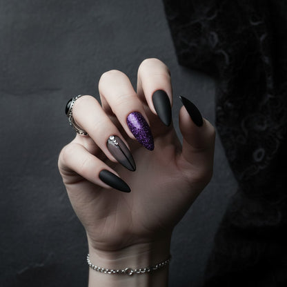 Auntie Cookies Nails: Almond-shaped press-on nails in matte black, sheer grey with rhinestones, purple glitter, and dark purple stripes.
