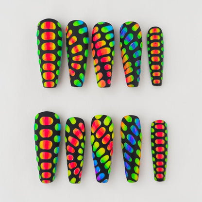 Auntie Cookies Nails: Black coffin press-on nails with a rainbow scale pattern. Features vibrant, multi-colored oval shapes against a matte black background.