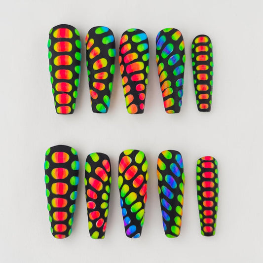Auntie Cookies Nails: Black coffin press-on nails with a rainbow scale pattern. Features vibrant, multi-colored oval shapes against a matte black background.