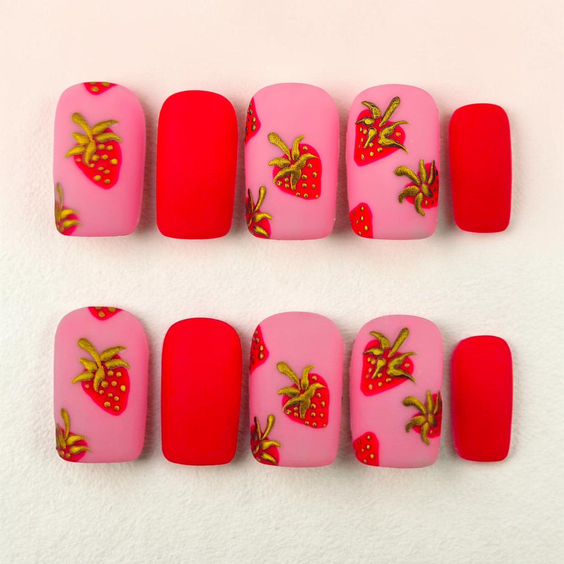 Auntie Cookies Nails matte pink and red press-on nails with strawberry designs and gold accents.