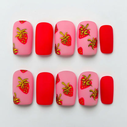 Auntie Cookies Nails matte pink and red press-on nails with gold and red strawberry designs.